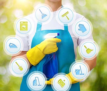 janitor in a blue apron don with yellow gloves, holding a blue spray can offering different cleaning services