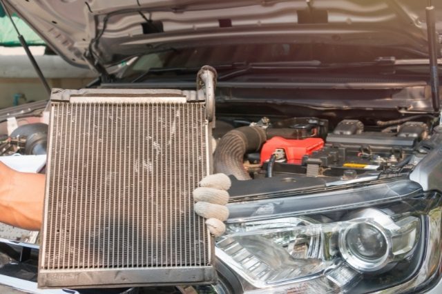 a repair man hold a car radiator while servicing a car